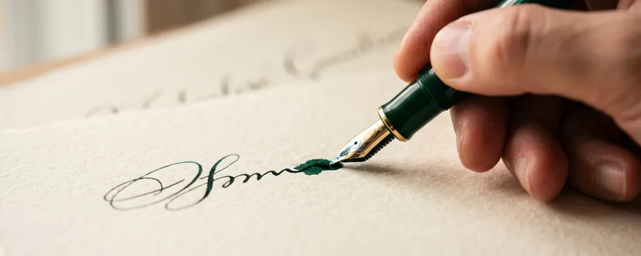 Hand signing a document with a fountain pen on heavy paper